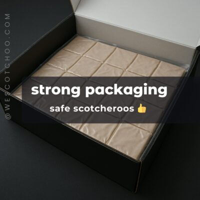 Open black shipping box displaying a vacuum-sealed package of 24 Scotcheroos, resting on a modern white marble countertop with minimal side gaps, emphasizing sturdy, gift-ready packaging.