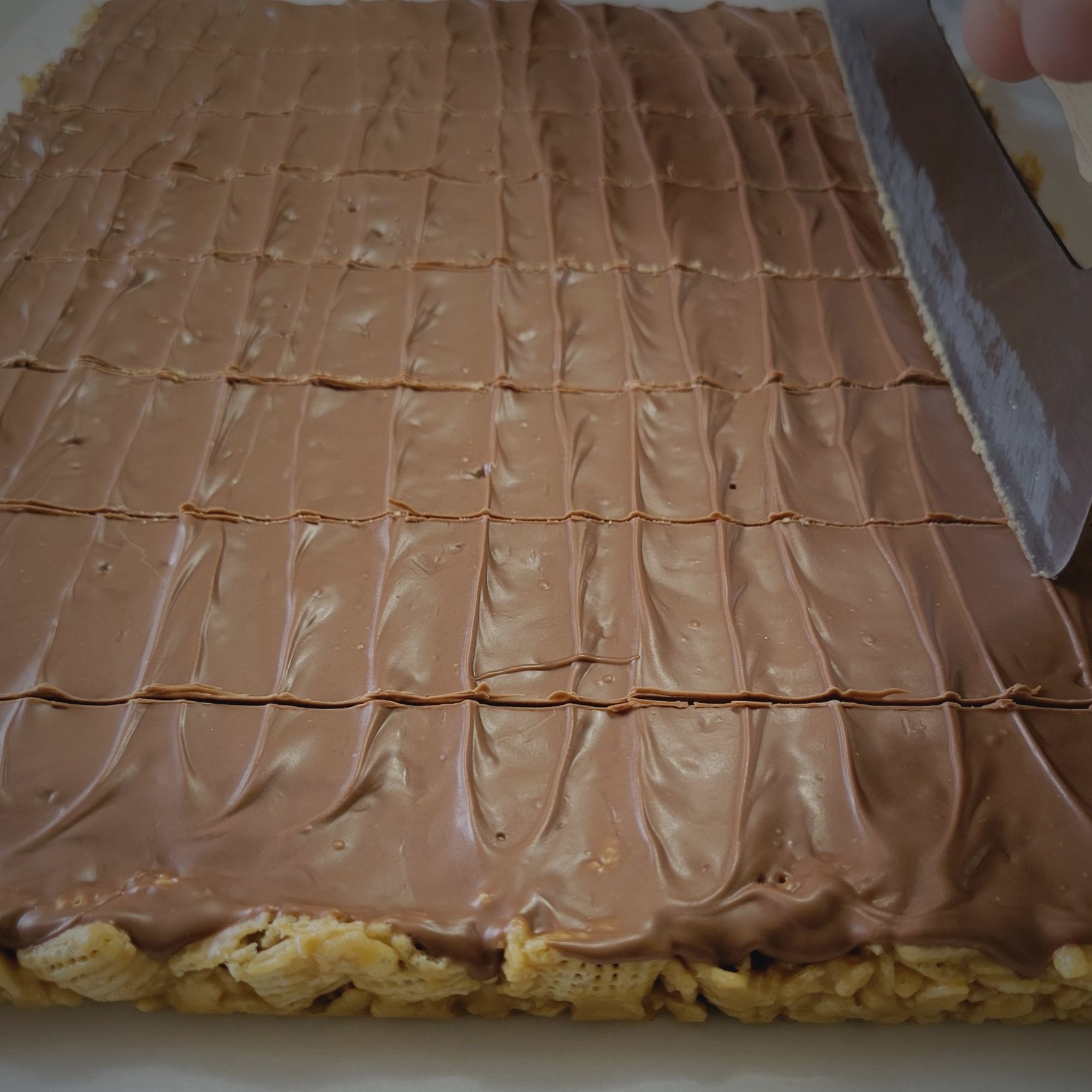 Pan of Scotcheroos being sliced into bars using the homemade scotcheroos recipe by weScotchoo.com – soft, chewy, and topped with chocolate and butterscotch.