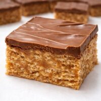 Warm close-up of homemade Scotcheroo bar showing thick chocolate layer and dense peanut butter rice crispy texture
