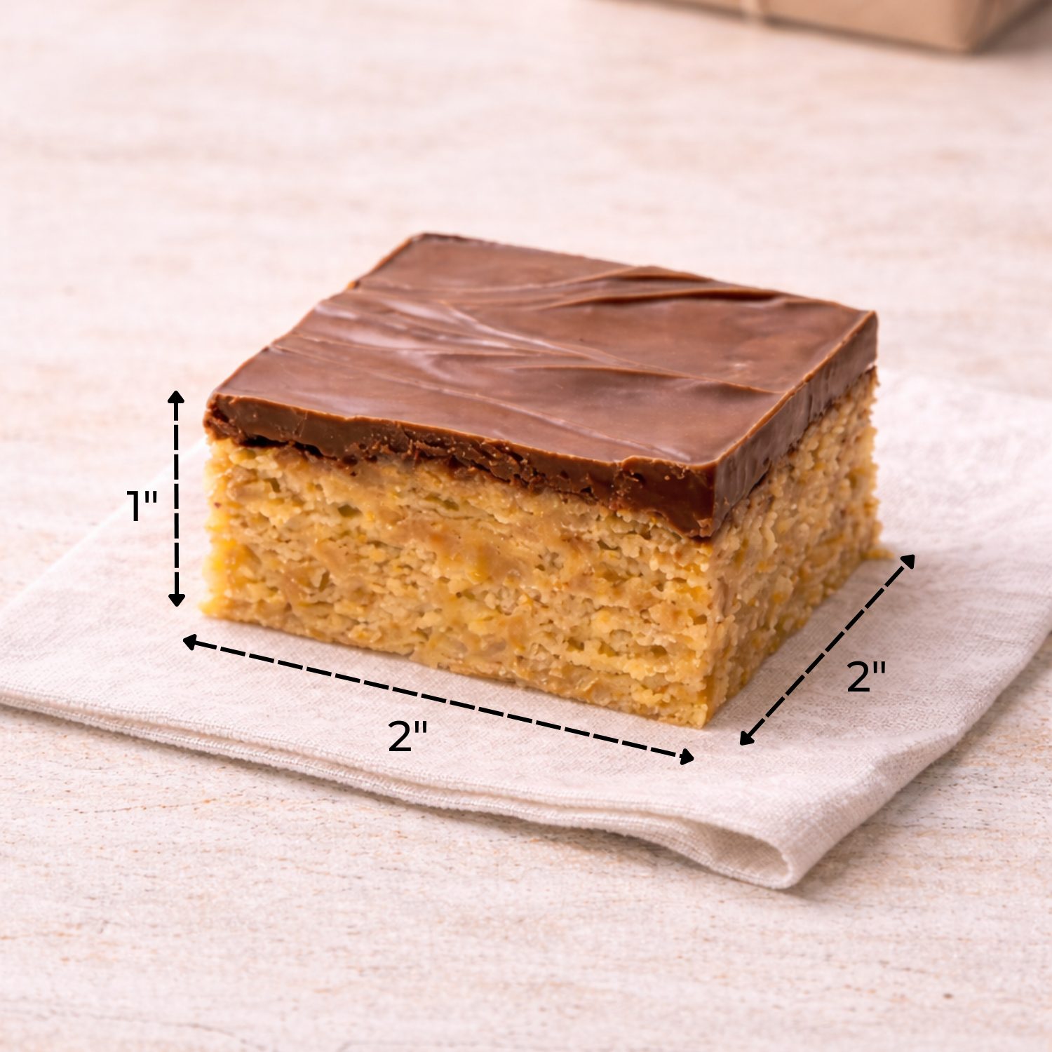 Size reference showing a 2x2 inch Scotcheroo bar with 1 inch height, layered peanut butter cereal base topped with thick chocolate and butterscotch.