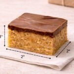 Size reference showing a 2x2 inch Scotcheroo bar with 1 inch height, layered peanut butter cereal base topped with thick chocolate and butterscotch.
