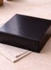 Glossy black Scotcheroo gift box closed and ready for shipping, displayed on a neutral linen surface with soft natural lighting. {{brizy_dc_image_alt imageSrc=