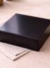 Glossy black Scotcheroo gift box closed and ready for shipping, displayed on a neutral linen surface with soft natural lighting.